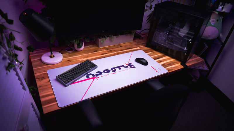 Wooden desk with a large mouse pad, keyboard, and mouse in a dark room.