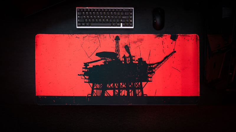 Red deskmat featuring a black offshore oil rig silhouette with a distressed industrial design on a dark desk setup.