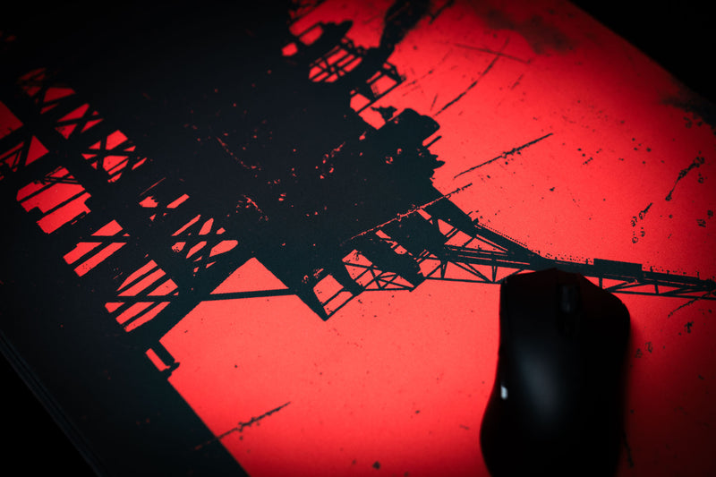 Detailed close-up of a red and black oil rig deskmat with a distressed industrial design and black gaming mouse.