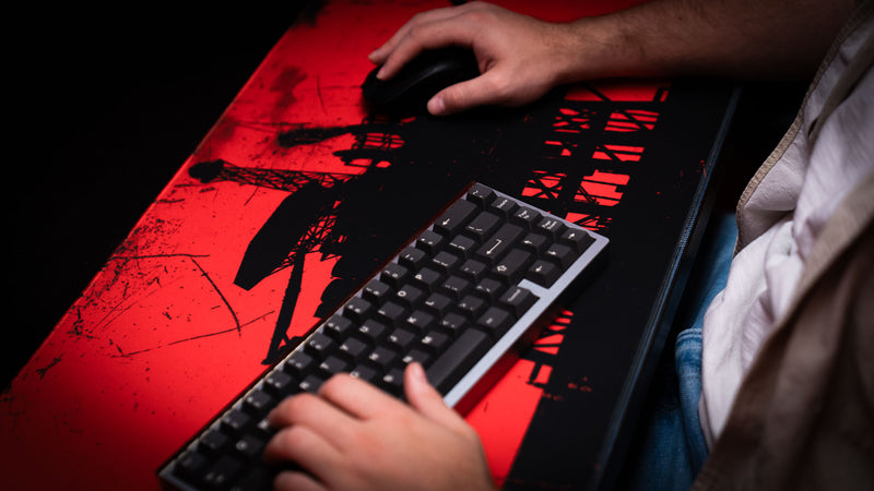 Red and black oil rig deskmat being used with a mechanical keyboard and gaming mouse in a dark desktop setup.