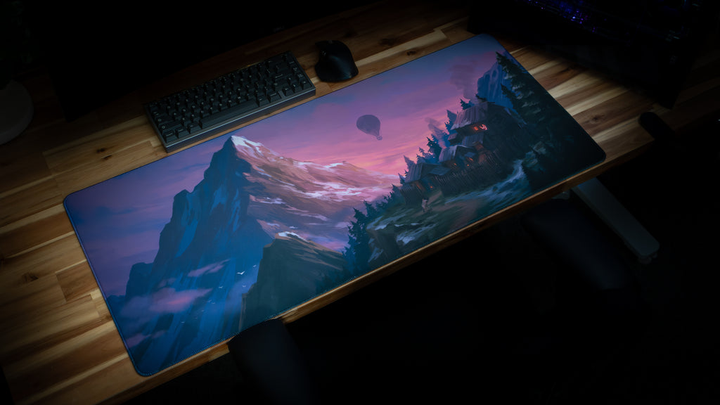 Desk setup with a large mouse pad featuring a scenic design of mountains and trees.