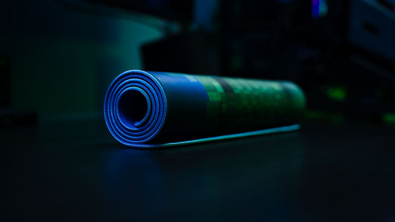 Rolled Adventure Begins XXL deskmat featuring stitched edges and a pixel-style forest design with blue ambient lighting.
