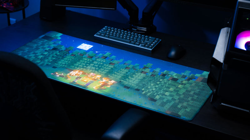 ApolloTV “Adventure Begins” deskmat displayed in a gaming setup featuring a pixel-style forest, moonlit sky, and friends gathered around a campfire.