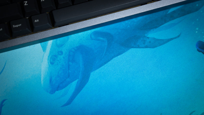 Close-up of the leviathan's head and blue fabric surface on Alidove's Lurking Leviathan deskmat beside a keyboard.