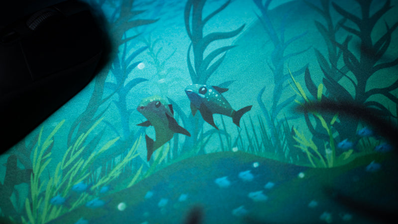 Two small sea creatures among kelp on Alidove's Lurking Leviathan deskmat, with a black mouse at the left.