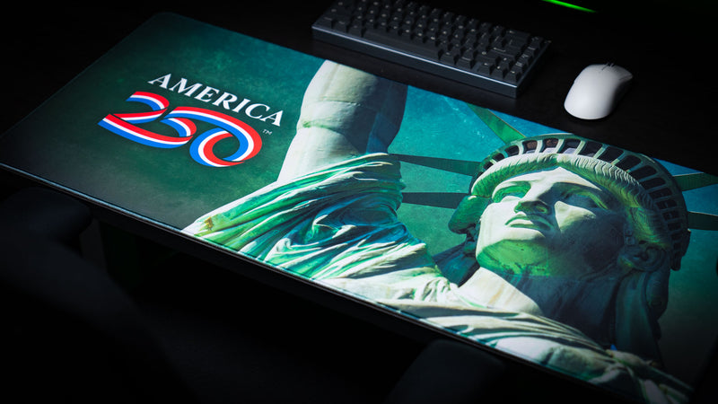 Premium America 250 Statue of Liberty deskmat displayed on a desktop, featuring a dramatic close-up of the Statue of Liberty, vibrant America 250 logo, rich green tones, and durable stitched edges for gaming and office setups.