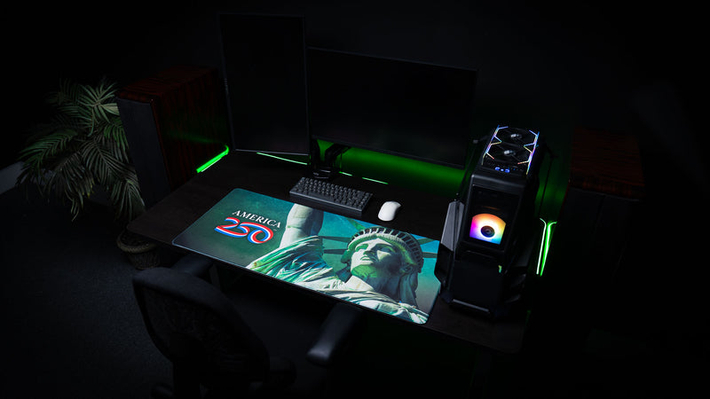 Angled desktop setup featuring the America 250 Statue of Liberty gaming deskmat with a striking close-up of the Statue of Liberty, bold America 250 logo, vibrant green tones, and premium stitched-edge construction.
