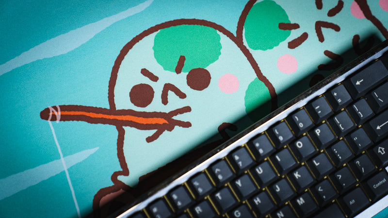 Fishing frog character close-up beside a keyboard on the blue Angyfrog Frogs on a Log desk mat