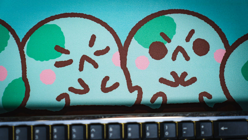 Close-up of two green frog characters on the Angyfrog Frogs on a Log desk mat above a keyboard