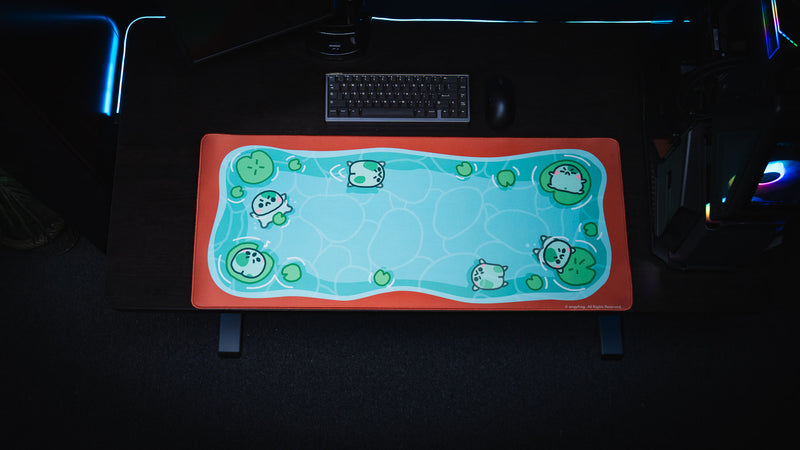 Top-down dark desk setup with keyboard above the colorful Angyfrog The Pond desk mat