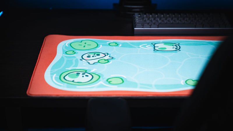 Front angled view of the Angyfrog The Pond desk mat beneath a keyboard on a dark desk