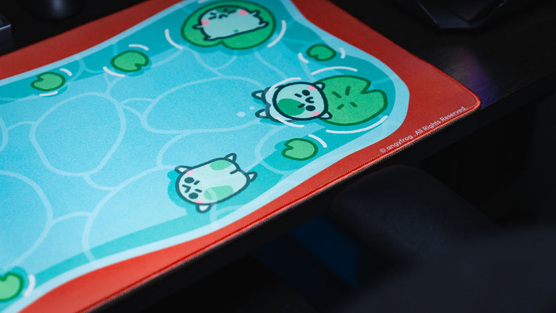 Angled detail of three frog characters floating on lily pads across Angyfrog The Pond desk mat