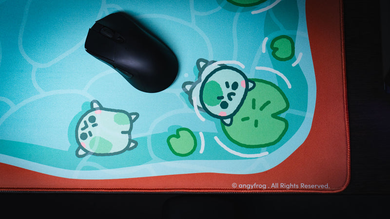 Black mouse beside two pond frogs and the Angyfrog artist mark on The Pond desk mat