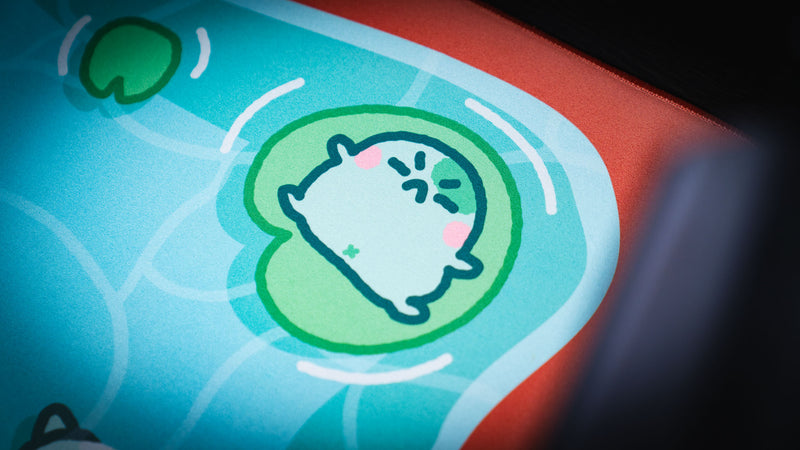 Close-up of a sleeping frog floating on a lily pad in the Angyfrog The Pond desk mat artwork