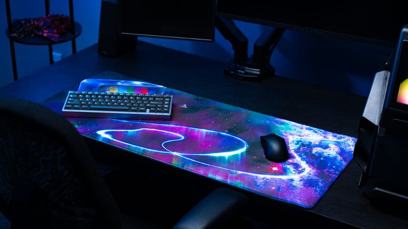 Gaming setup featuring the ApolloTV “Cosmic TV” deskmat with vibrant galaxy artwork, neon space effects, keyboard, and gaming mouse.