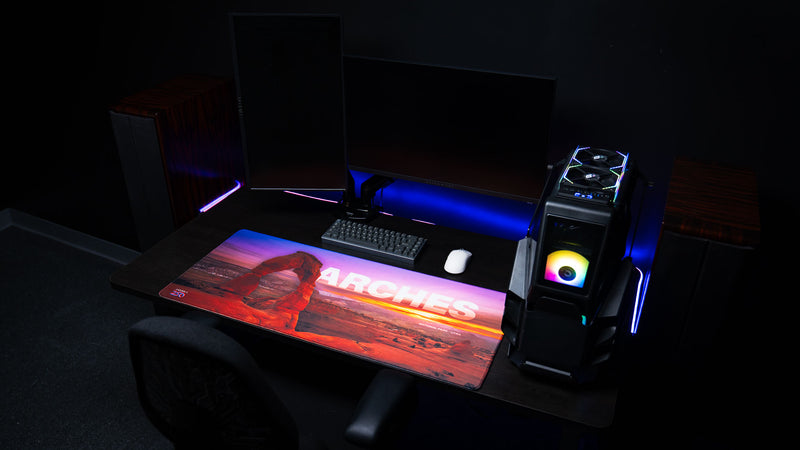 Arches National Park premium deskmat displayed in a modern gaming setup, featuring Delicate Arch photography, vibrant sunset colors, and a large extended gaming surface.