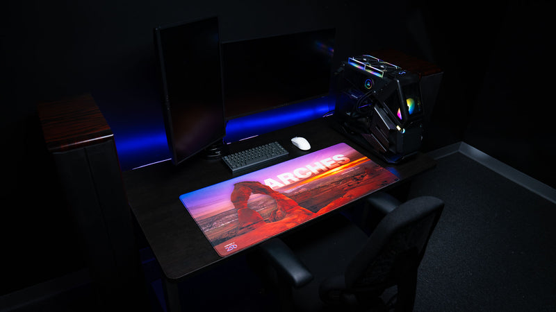 Arches National Park premium deskmat displayed in a modern gaming setup featuring Delicate Arch at sunset, an extended gaming surface, and vibrant landscape photography.