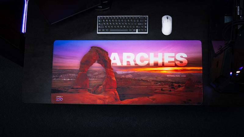 Top-down view of the Arches National Park premium deskmat featuring Delicate Arch at sunset, vibrant landscape photography, stitched edges, and a smooth gaming surface.