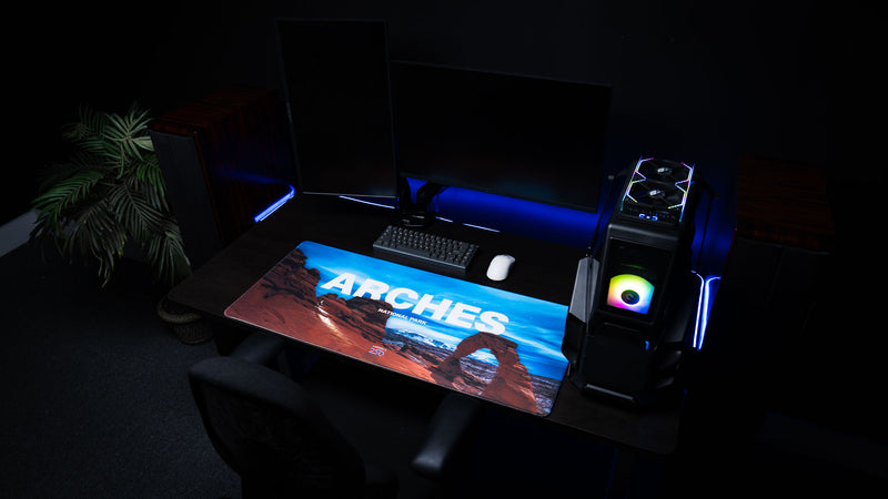 Arches National Park America 250 deskmat displayed in an RGB gaming station with Delicate Arch artwork, keyboard, mouse, and PC setup.