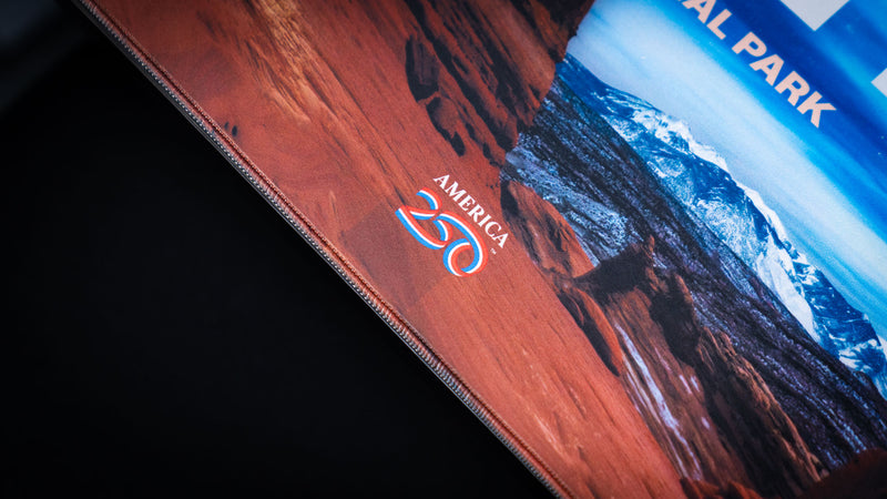 Arches deskmat detail featuring red rock texture, America 250 branding, blue mountain scenery, and premium stitched border.