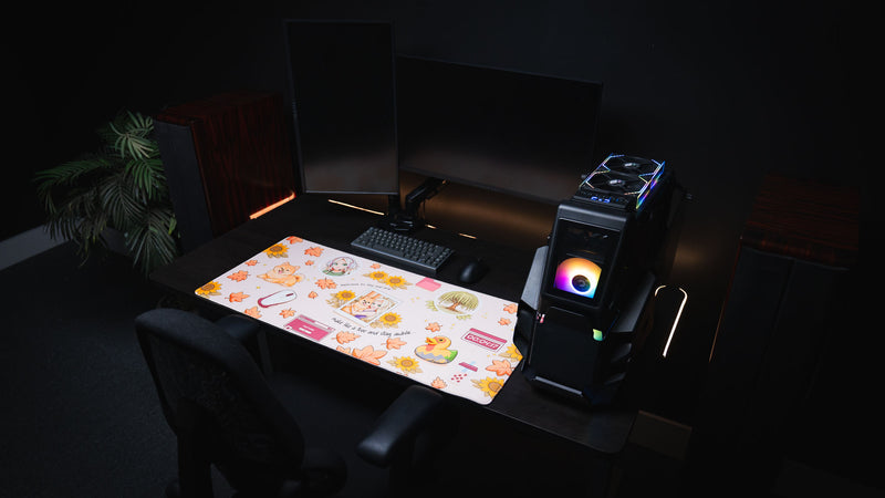 Complete gaming desk setup featuring the Cozy Desk deskmat with autumn-themed illustrations, dual monitors, RGB gaming PC, mechanical keyboard, and a cozy fall-inspired workspace.
