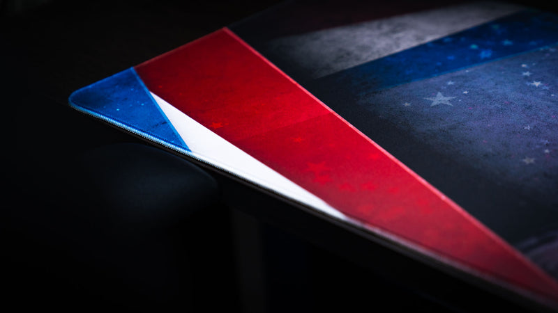 Close-up of the Bald Eagle America 250 deskmat showing patriotic red, white, and blue stripe artwork, subtle star texture, and stitched edge detail.
