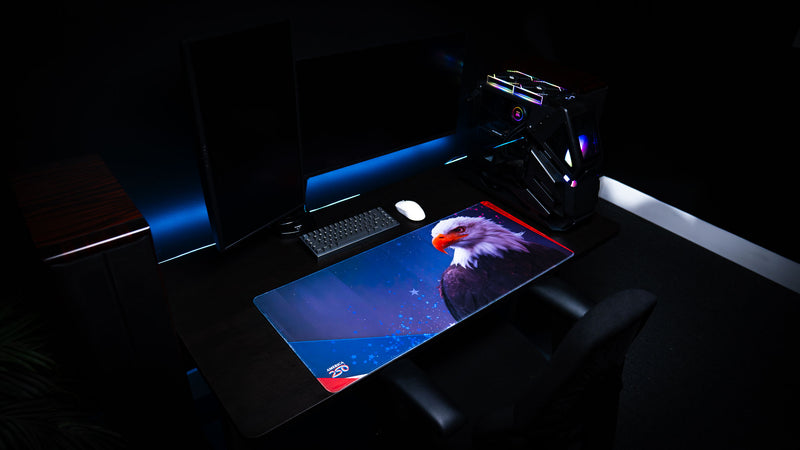 Angled view of the Bald Eagle Blue America 250 deskmat in an RGB gaming setup with eagle artwork, keyboard, mouse, and PC.
