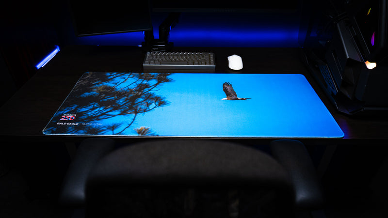 Close-up lifestyle view of the Bald Eagle in Flight deskmat on a desktop setup, showcasing a soaring bald eagle over a vivid blue Utah sky from the America 250 collection.