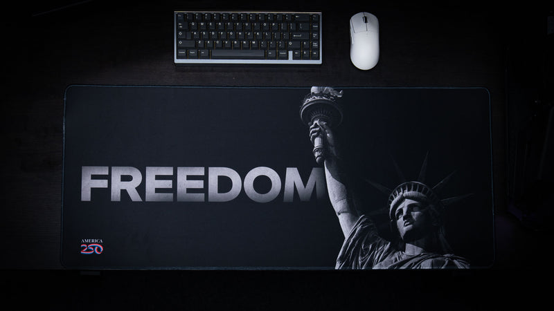 Black and white Freedom deskmat featuring the Statue of Liberty with bold "FREEDOM" typography, premium stitched edges, oversized extended gaming mouse pad, and minimalist patriotic artwork.