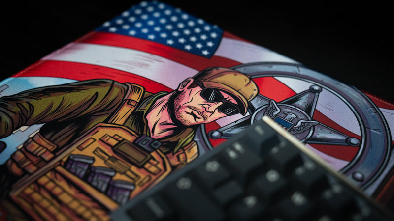 Close-up of the BobbyRayGray BRG Loading deskmat featuring an American sheriff-inspired character against a U.S. flag backdrop with detailed comic-style artwork.