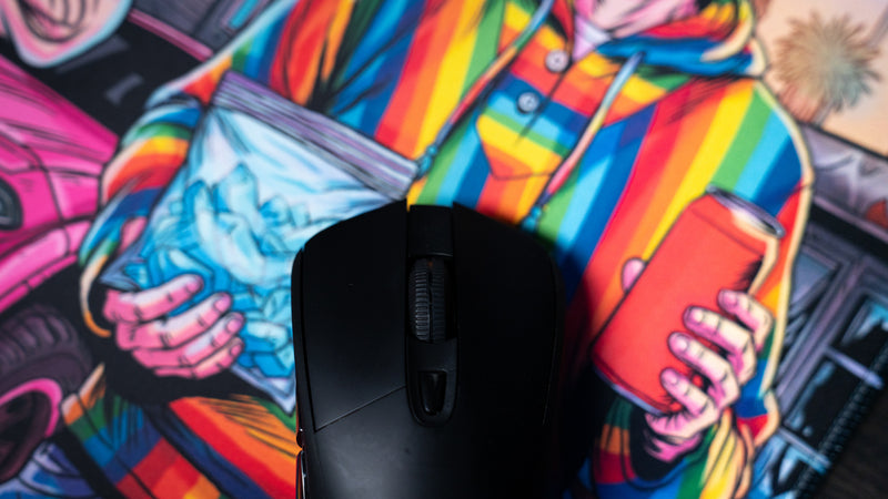 Gaming mouse on the BobbyRayGray BRG Loading deskmat highlighting the colorful comic-style artwork and smooth premium cloth surface for precise mouse tracking.