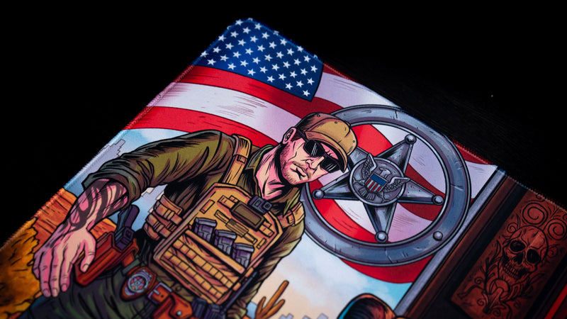 Close-up of the BobbyRayGray BRG Loading deskmat featuring a tactical character in front of an American flag with bold comic-style artwork and vibrant colors.