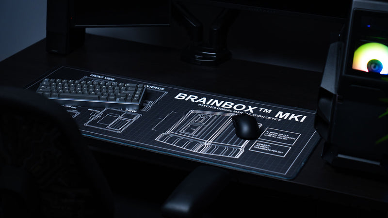 BRAINBOX MK1 deskmat displayed in a gaming setup featuring Rust-inspired blueprint artwork, technical schematics, and premium extended mousepad coverage.