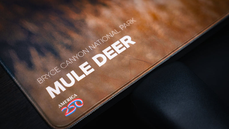 Close-up of the Bryce Canyon Mule Deer America 250 deskmat highlighting the premium stitched edge, bold typography, and detailed wildlife photography.