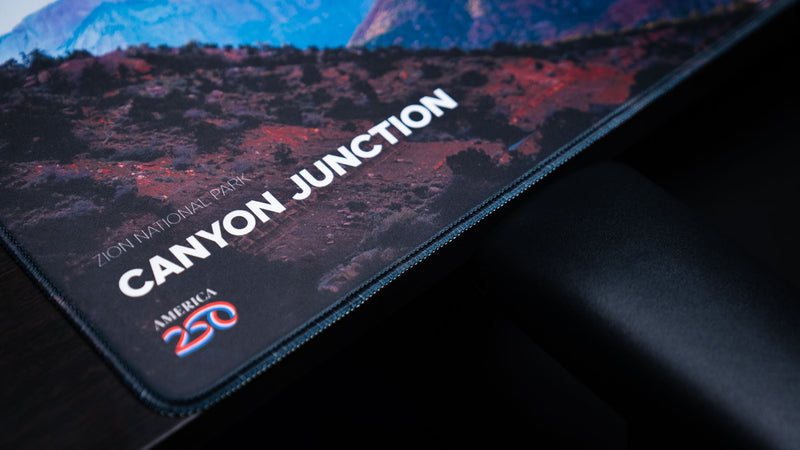 Close-up of the Canyon Junction deskmat highlighting Zion National Park branding, the America 250 logo, premium stitched edges, and crisp HD print quality.