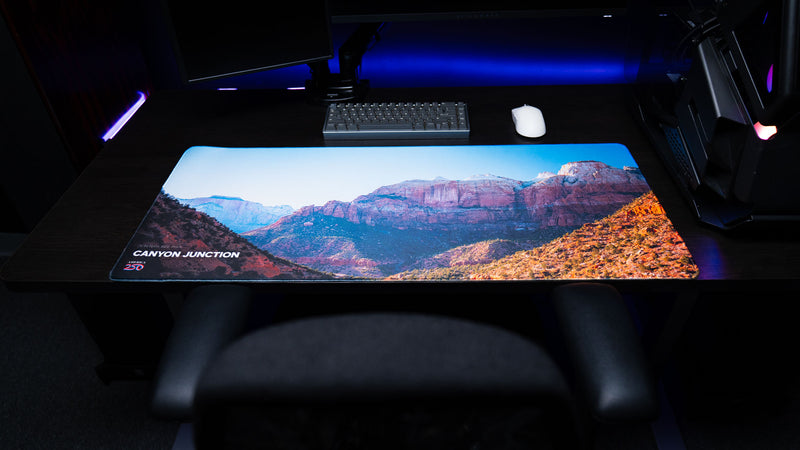 Wide view of the Canyon Junction deskmat featuring Zion National Park's dramatic canyon landscape, premium stitched edges, vibrant HD photography, and a modern gaming setup.