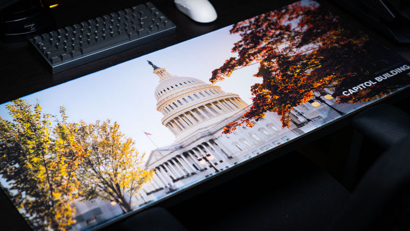 Angled lifestyle photo of the Capitol Building deskmat featuring the U.S. Capitol surrounded by vibrant autumn trees on a premium extended gaming mouse pad with stitched edges.