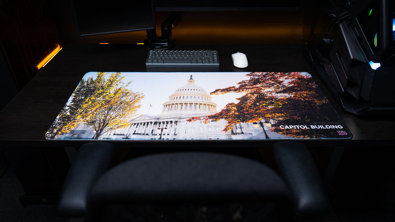 Full desk setup featuring the Capitol Building deskmat with the U.S. Capitol framed by autumn foliage, displayed as a premium extended gaming mouse pad with vibrant high-definition artwork and stitched edges.