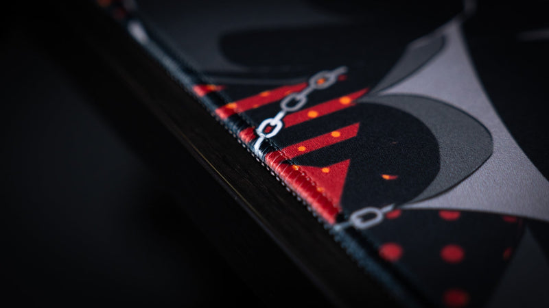 Close-up of the stitched edge and red graphic detail on the CelisEris Brand Risk gaming deskmat