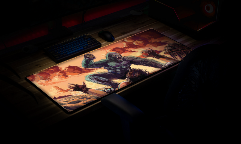 CocoKong gaming deskmat displayed on a desktop setup, featuring a giant gorilla attacking a survivor in a Rust-inspired beach scene at sunset.