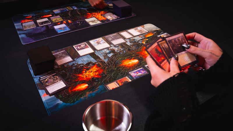 Player holding Magic: The Gathering cards over the Coralborn playmat during gameplay, showcasing the detailed fantasy ship artwork, vibrant colors, stitched edges, and premium surface for immersive TCG sessions.