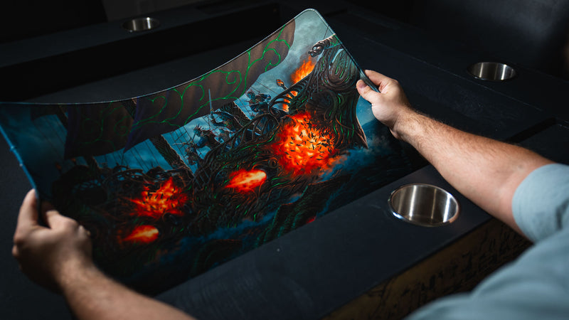 Hands flexing the Coralborn TCG playmat to showcase its flexible rubber base, premium stitched edges, and vibrant fantasy sea battle artwork.
