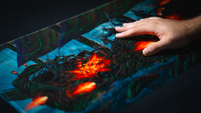 Hand gliding across the Coralborn playmat, highlighting the smooth premium fabric surface, intricate fantasy ship artwork, vivid colors, and durable stitched edges designed for competitive TCG play.