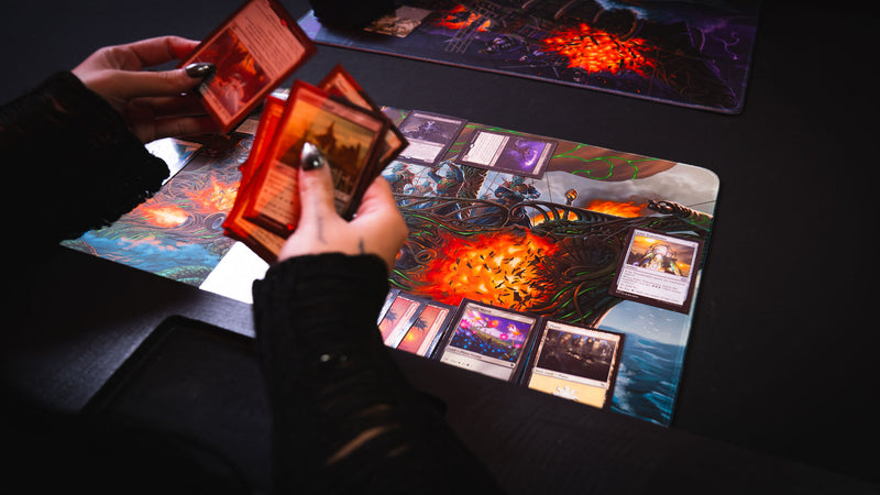 Player holding trading cards over the Coralborn playmat during a live TCG match, featuring detailed fantasy naval battle artwork, vibrant colors, stitched edges, and a premium tournament-ready play surface.