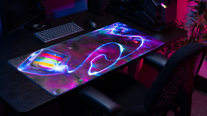 ApolloTV “Cosmic TV” deskmat displayed on a gaming desk with neon cosmic artwork, glowing energy trails, and a retro television floating through space.