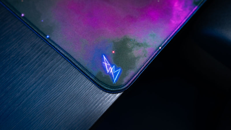 Close-up of the ApolloTV “Cosmic TV” deskmat corner featuring stitched edges, galaxy artwork, and glowing cosmic details on a dark desk.