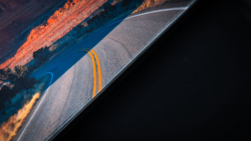 Close-up of the Courthouse Towers America 250 deskmat showing the desert road artwork, yellow lane lines, fabric texture, and stitched border.