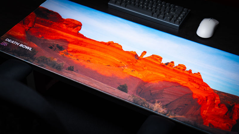 Angled view of the Death Bowl deskmat featuring the sweeping red sandstone basin and layered rock formations of Arches National Park in vibrant sunset light.