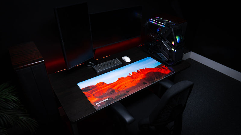Death Bowl deskmat showcased in a premium PC gaming setup, featuring the striking red sandstone basin of Arches National Park with vivid desert photography and stitched edges.