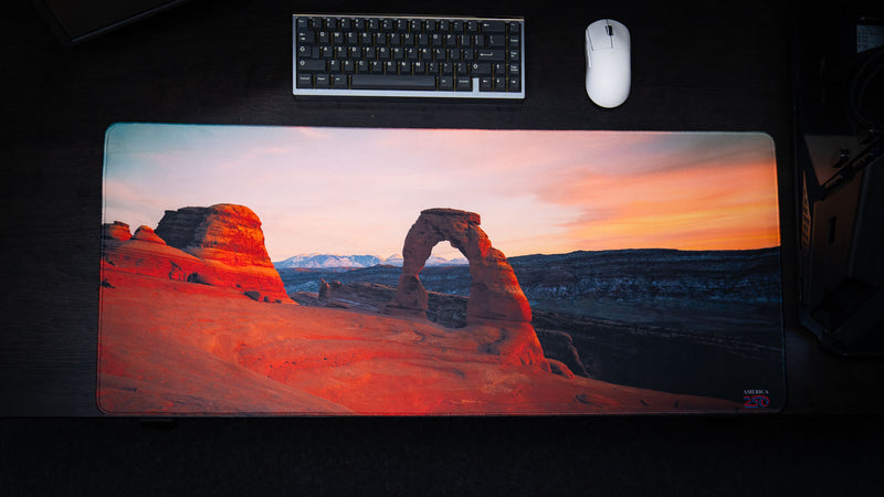 Top-down view of the Delicate Arch premium deskmat featuring Arches National Park at sunrise with vivid landscape photography, stitched edges, and a smooth extended gaming surface.